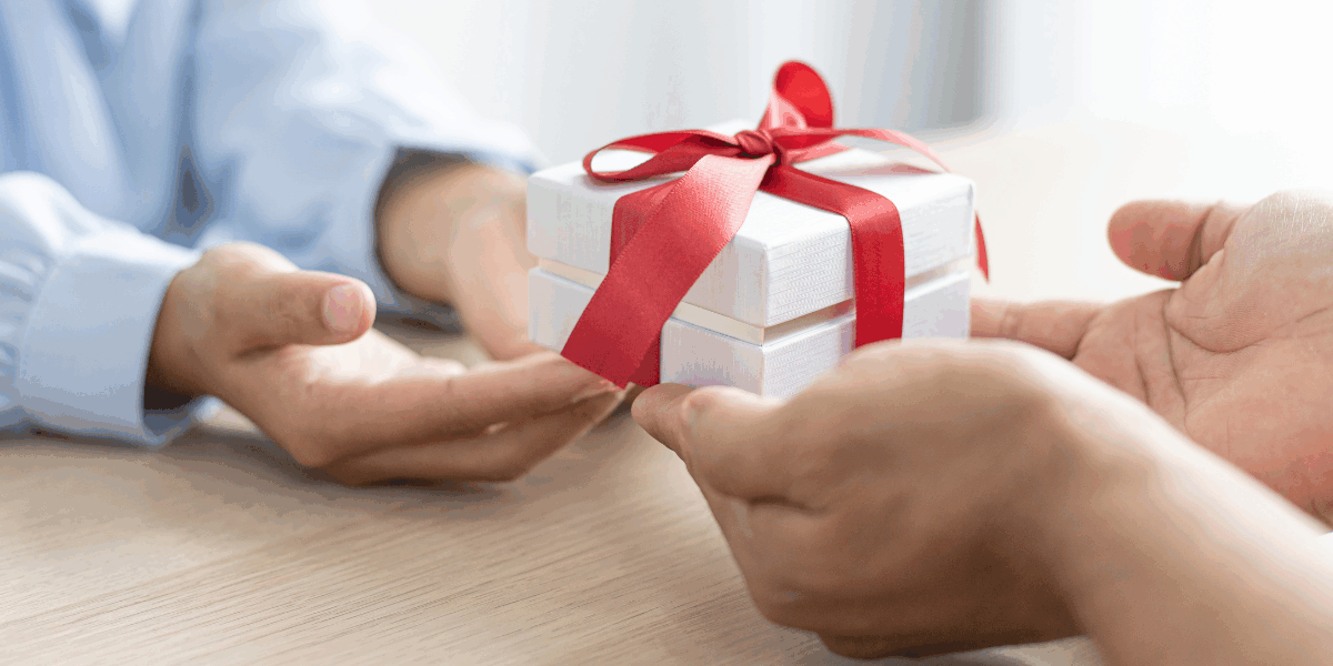 2 people exchanging a white gift box with red ribbon