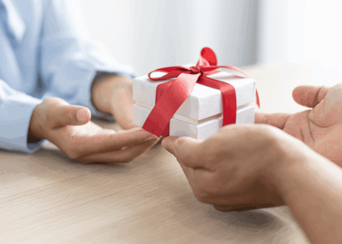 2 people exchanging a white gift box with red ribbon