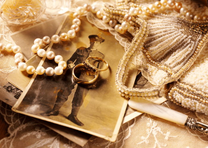 Collection of sentimental antique items: old black and white photograph, pearl necklace, lace, gold rings, beaded purse