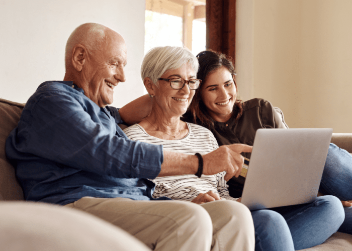 older mom and dad with adult child sitting on a couch looking at a laptop