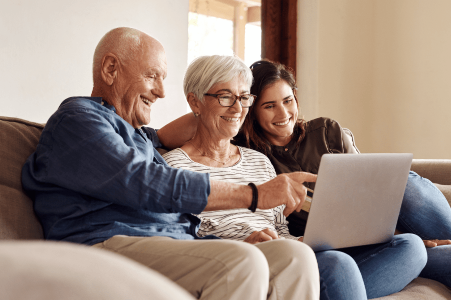 older mom and dad with adult child sitting on a couch looking at a laptop